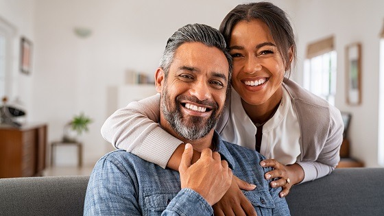 Portrait of multiethnic couple embracing and looking at camera sitting on sofa.